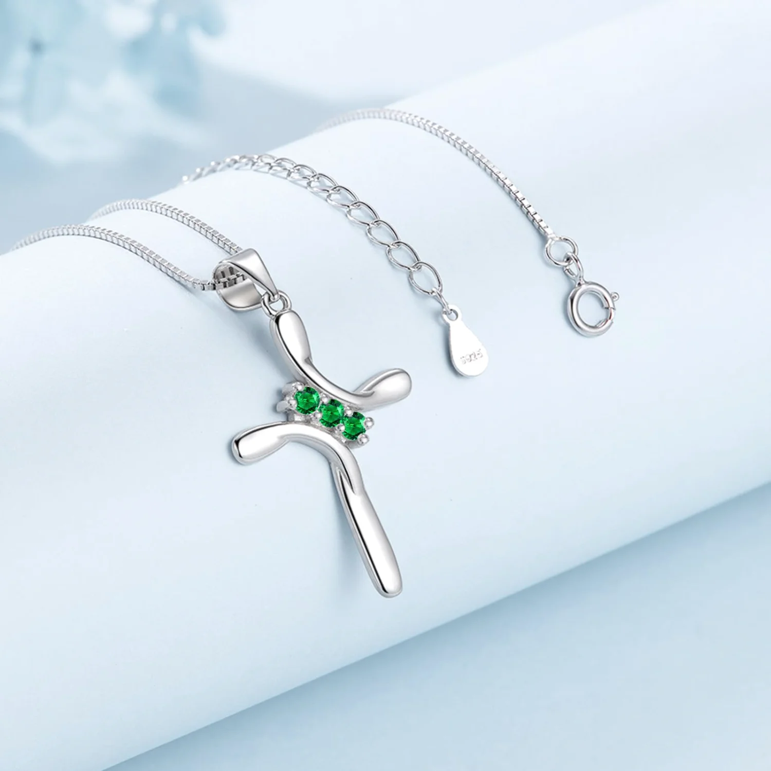 The May cross pendant with a green stone, worn on a neck