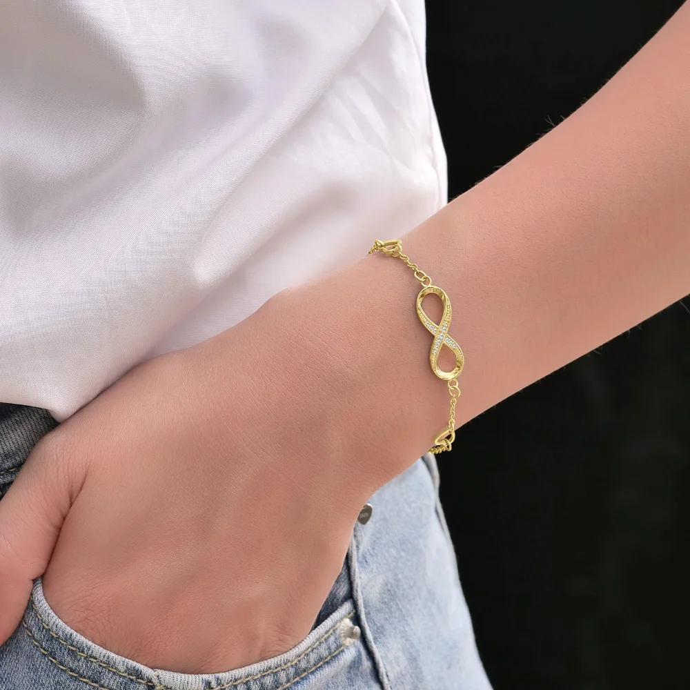 The gold infinity bracelet on a wrist against denim